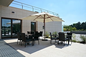 An outdoor patio with a table and chairs, a large umbrella, and a building with a glass door and windows.