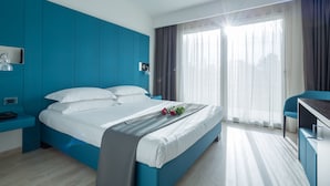 Una habitación de hotel moderna con una cama grande, un escritorio y vistas a la ciudad a través de cortinas translúcidas.