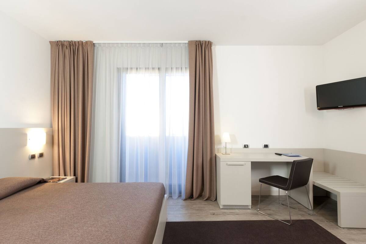 A hotel room with a bed, desk, chair, TV, and curtains.