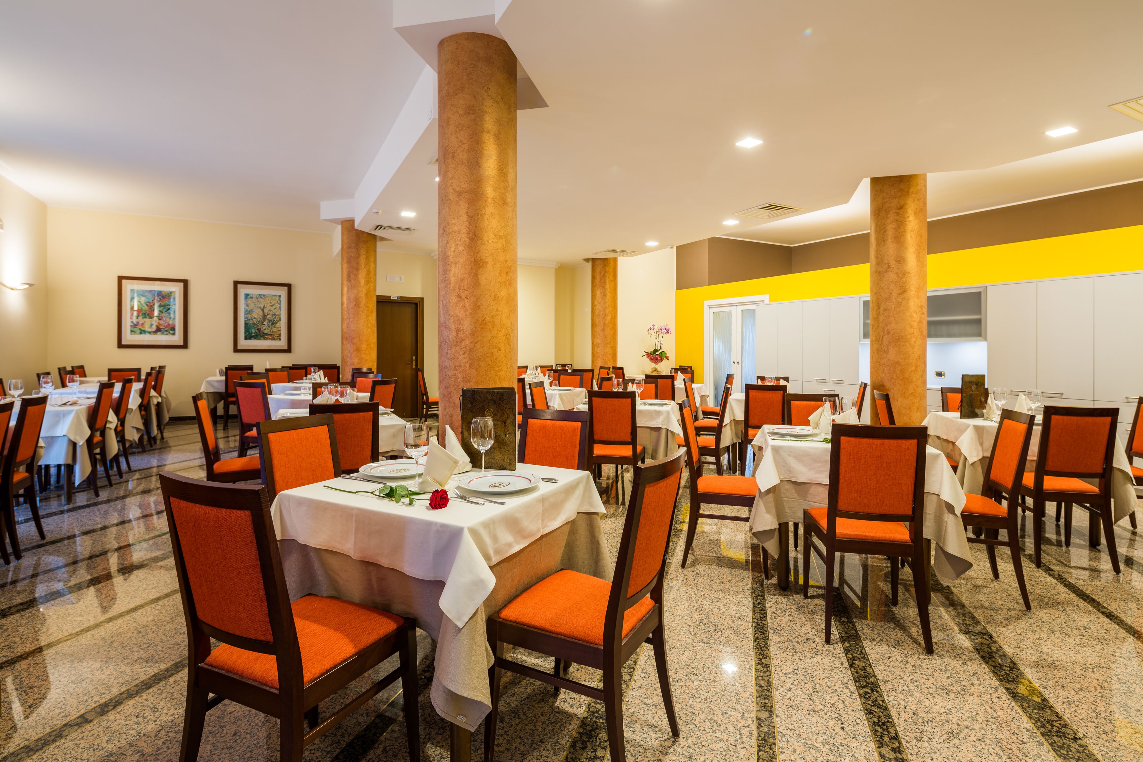 A dining area with tables set for multiple guests, featuring orange chairs and white tablecloths.
