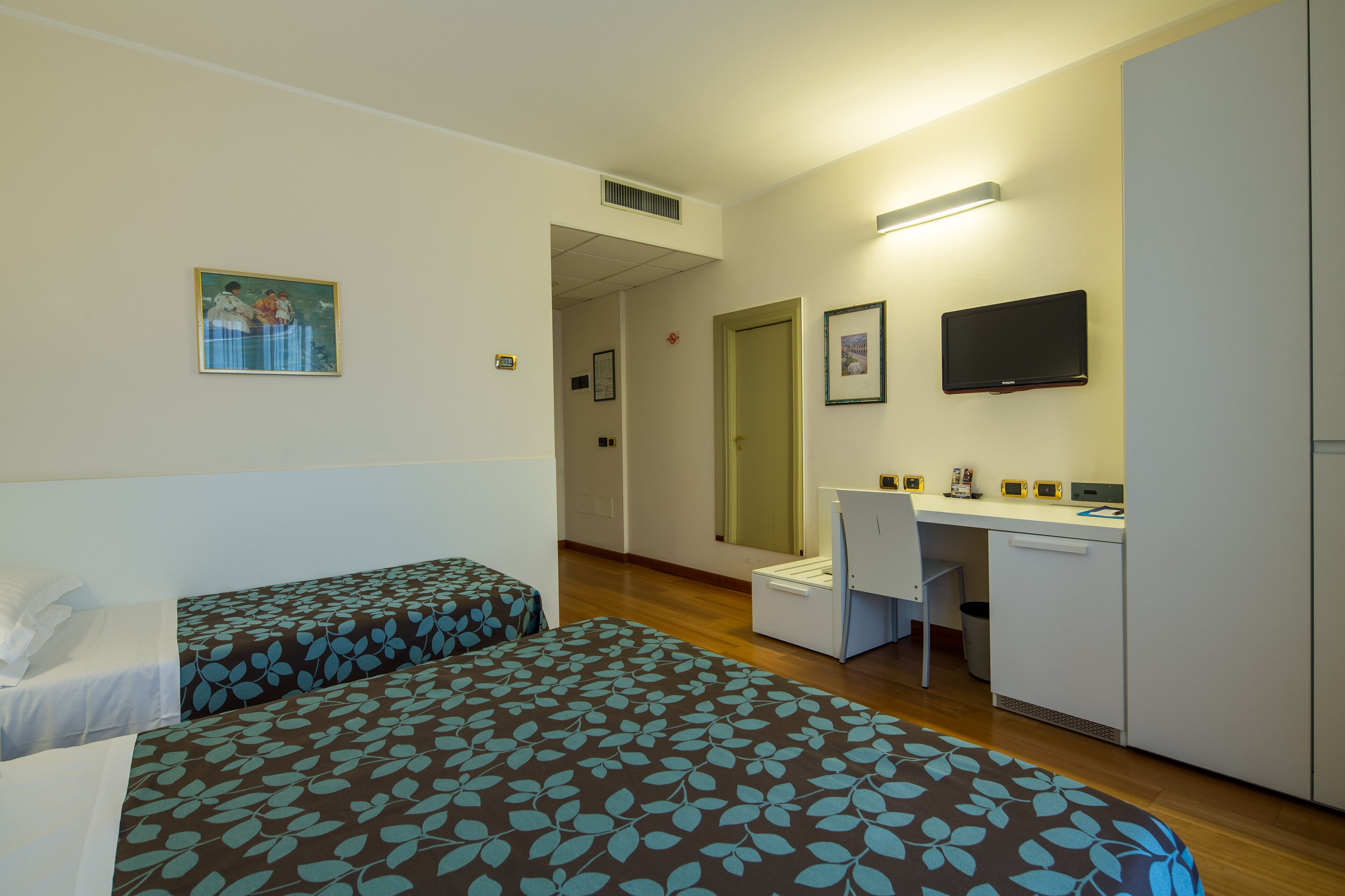 A hotel room with two beds, a desk, a chair, a television, and a mirror.