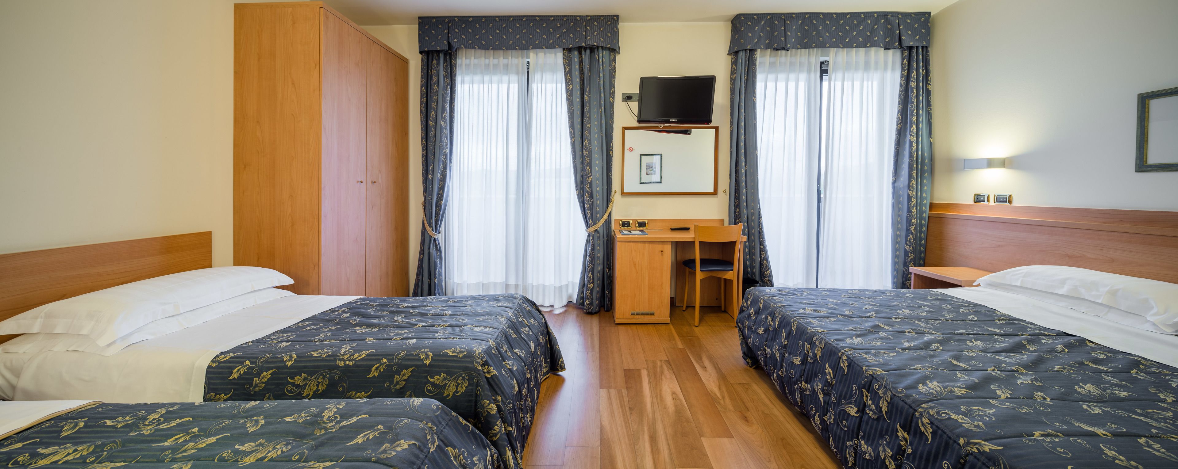 A hotel room with two beds, a desk, a TV, and a wardrobe.