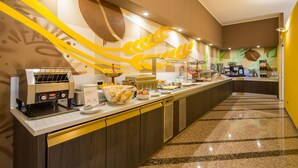 Una barra amplia con una máquina de café, un bol de pasteles y diversas opciones para el desayuno.
