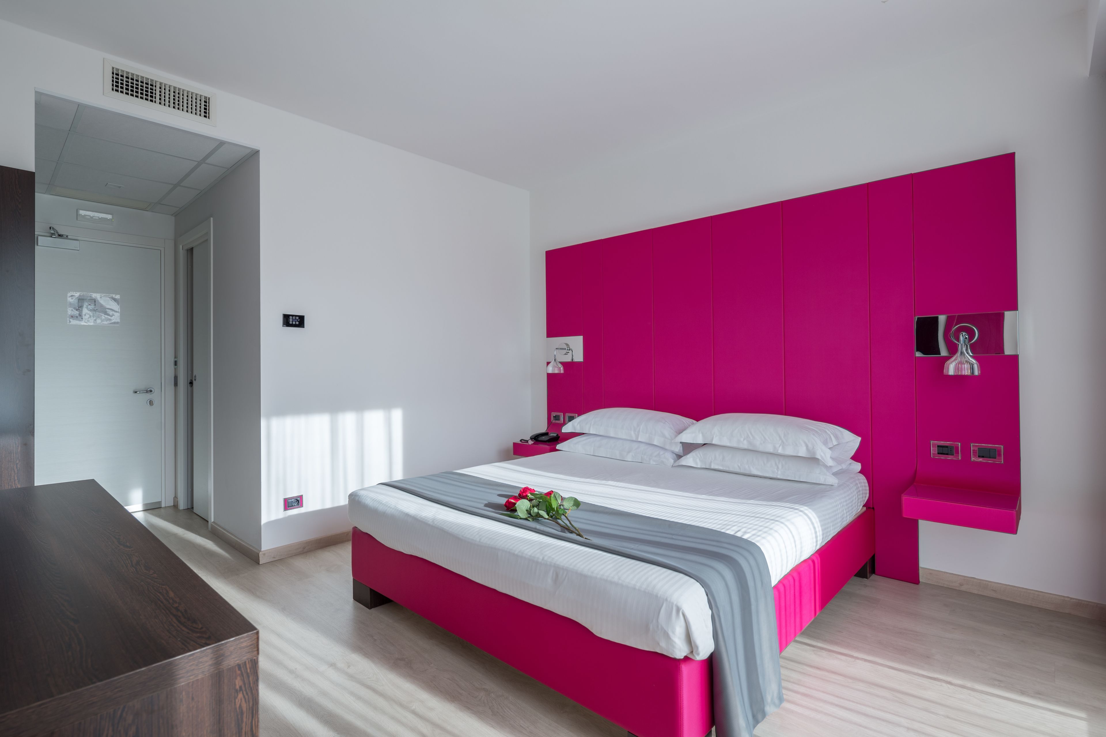 A modern bedroom with a bright pink headboard, a wooden bedside table, and a bed with white linens.