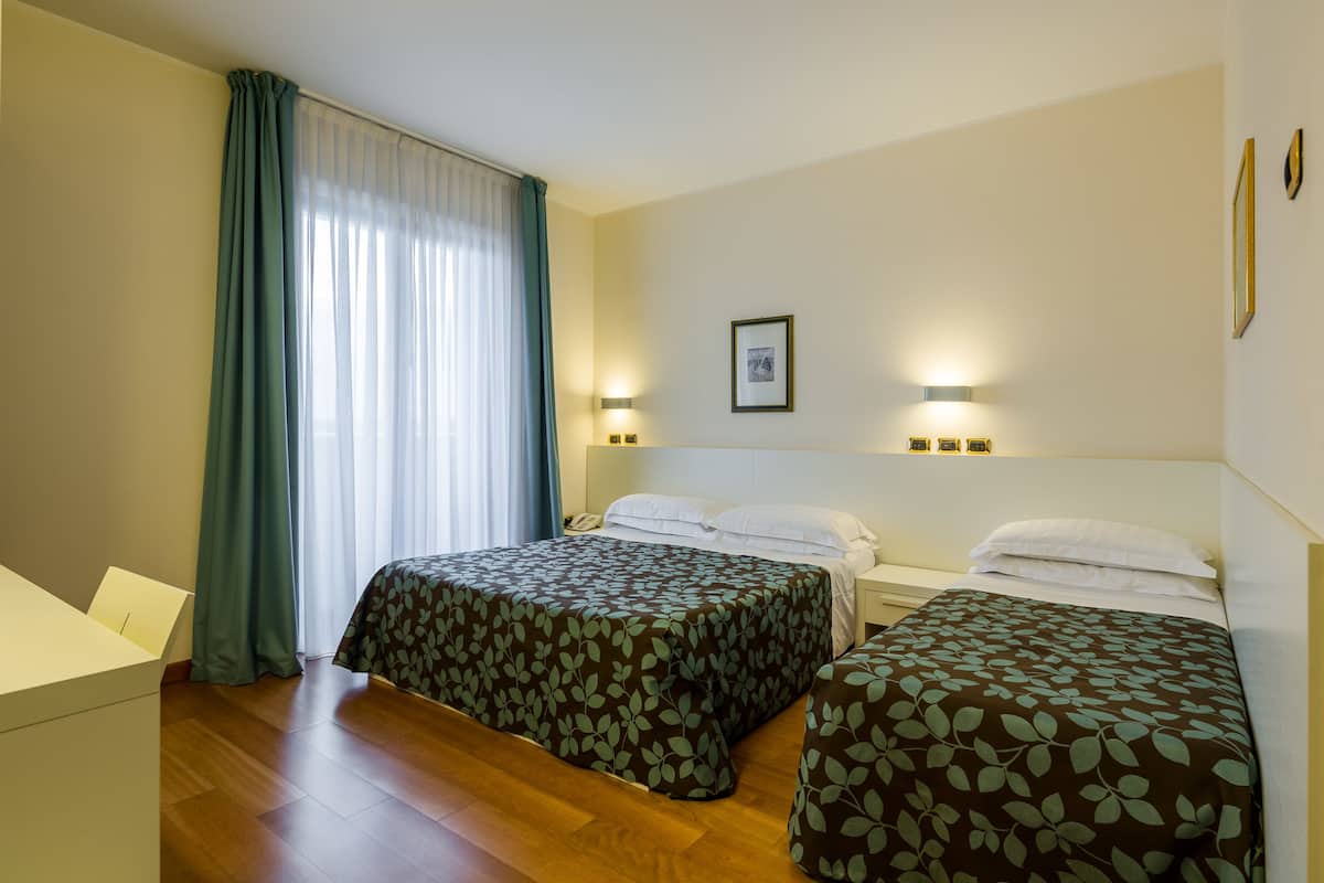 A hotel room with two beds, a desk, and a window with curtains.