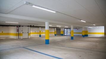 Un vaste espace de stationnement intérieur aux murs blancs et jaunes, aux piliers bleus et jaunes, et doté d’un éclairage plafond clair.