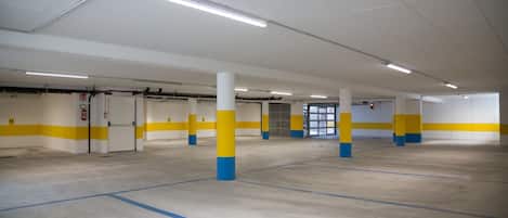 A spacious indoor parking area with white and yellow walls, blue and yellow pillars, and clear ceiling lighting.