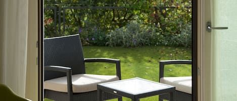 Una puerta corrediza de vidrio da a un patio exterior con mobiliario de mimbre y una silla verde.