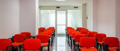 A conference room with rows of orange chairs, a polished floor, and a bright ceiling light.