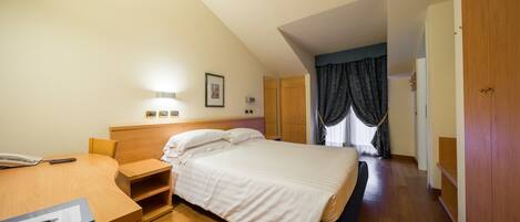 A hotel room with a bed, bedside table, lamp, and a desk with a chair.