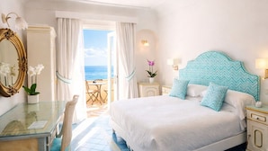 Une chambre avec un grand lit, un bureau et une chaise. On peut admirer l’océan à travers une porte.
