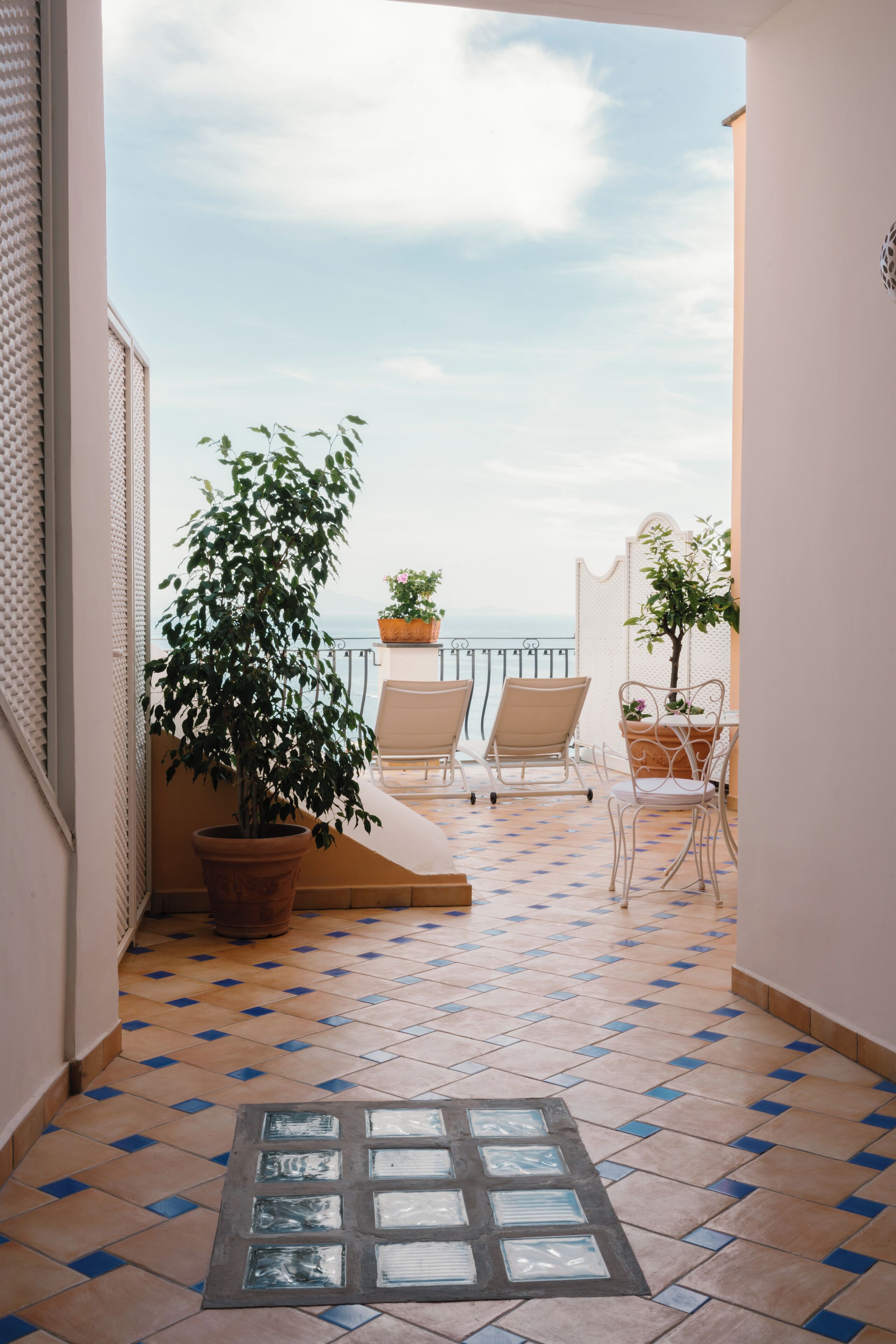 A balcony with a view of the sea, two chairs, and potted plants.