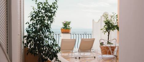 A balcony with a view of the sea, two chairs, and potted plants.