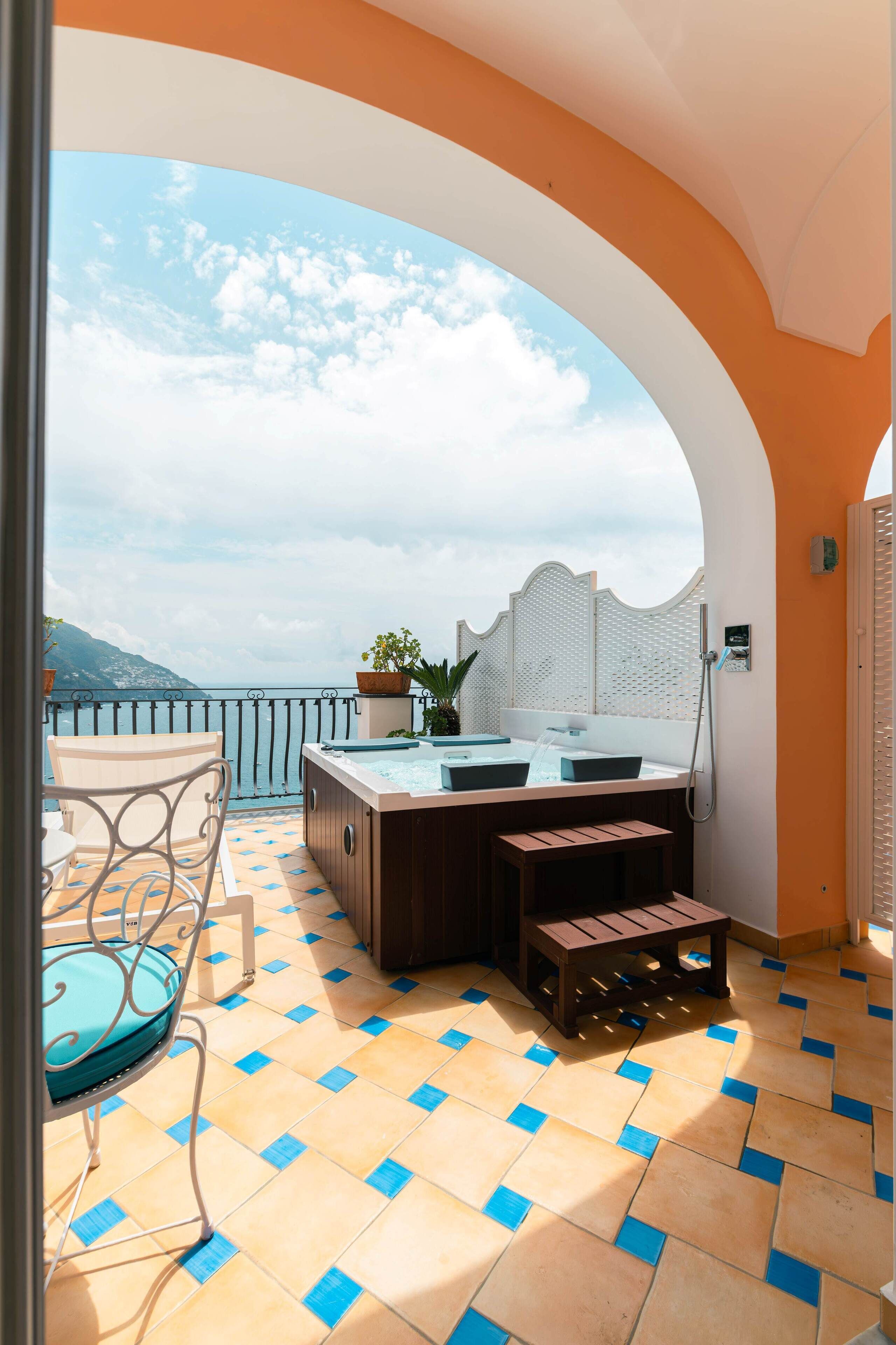 A balcony with a hot tub, seating, and a view of the sea.