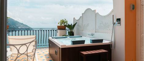 A balcony with a hot tub, seating, and a view of the sea.