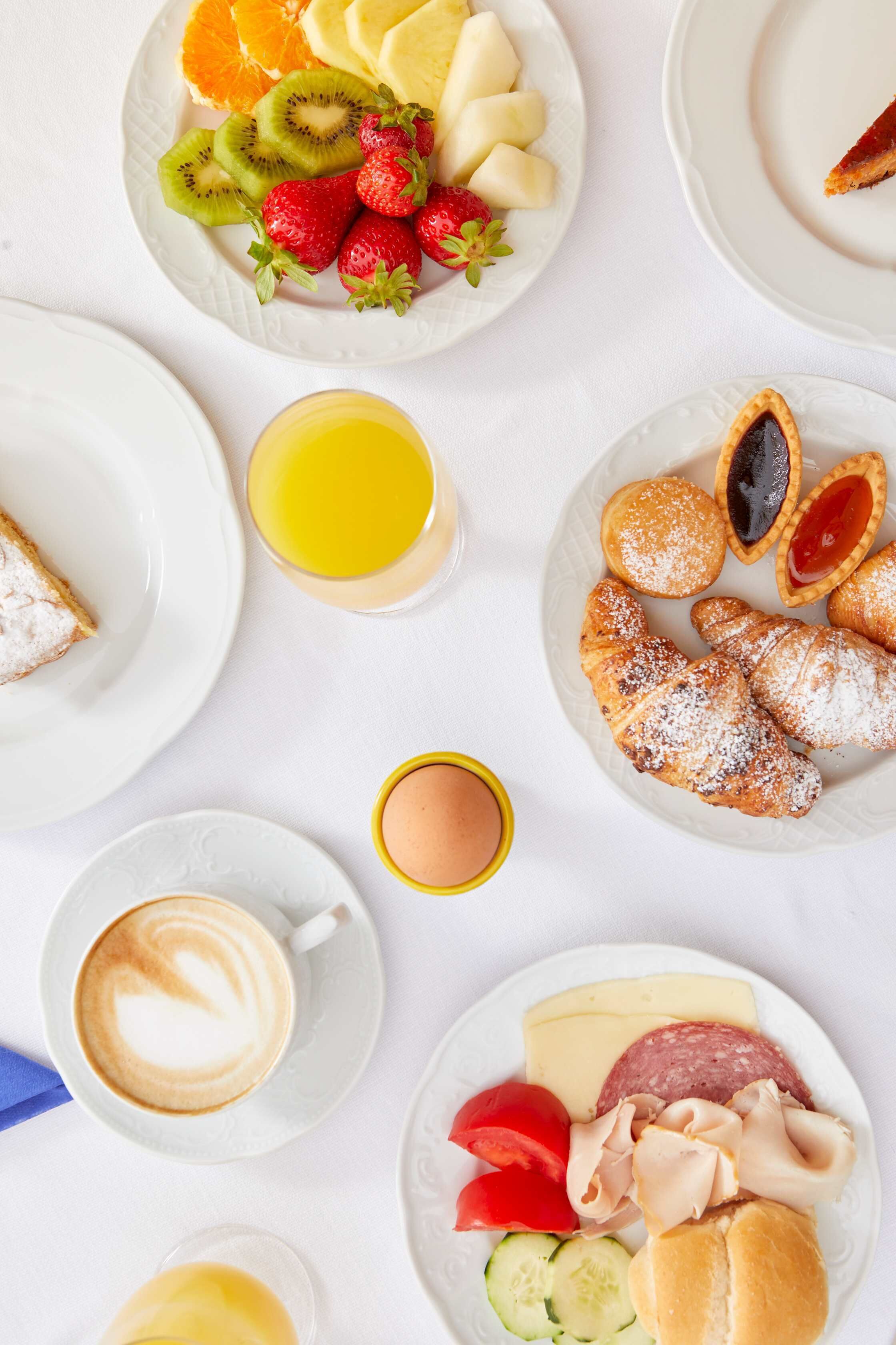 A breakfast setting with plates of fruit, pastries, and a coffee cup.