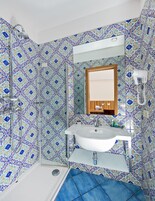 Un baño con un lavamanos blanco, un espejo encima y una zona de ducha.