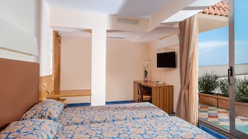 A bedroom with a large bed, a desk, a TV, and a balcony with a tiled floor.