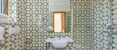 Une salle de bain avec un lavabo, des toilettes et une douche, le tout de couleur blanche. Les murs sont recouverts de carreaux disposés selon un motif géométrique.