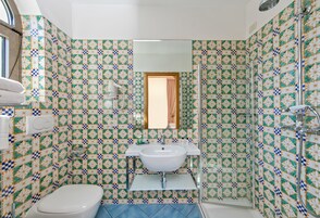 Un baño con lavamanos, inodoro y ducha blancos. Las paredes están cubiertas de azulejos con un diseño geométrico.