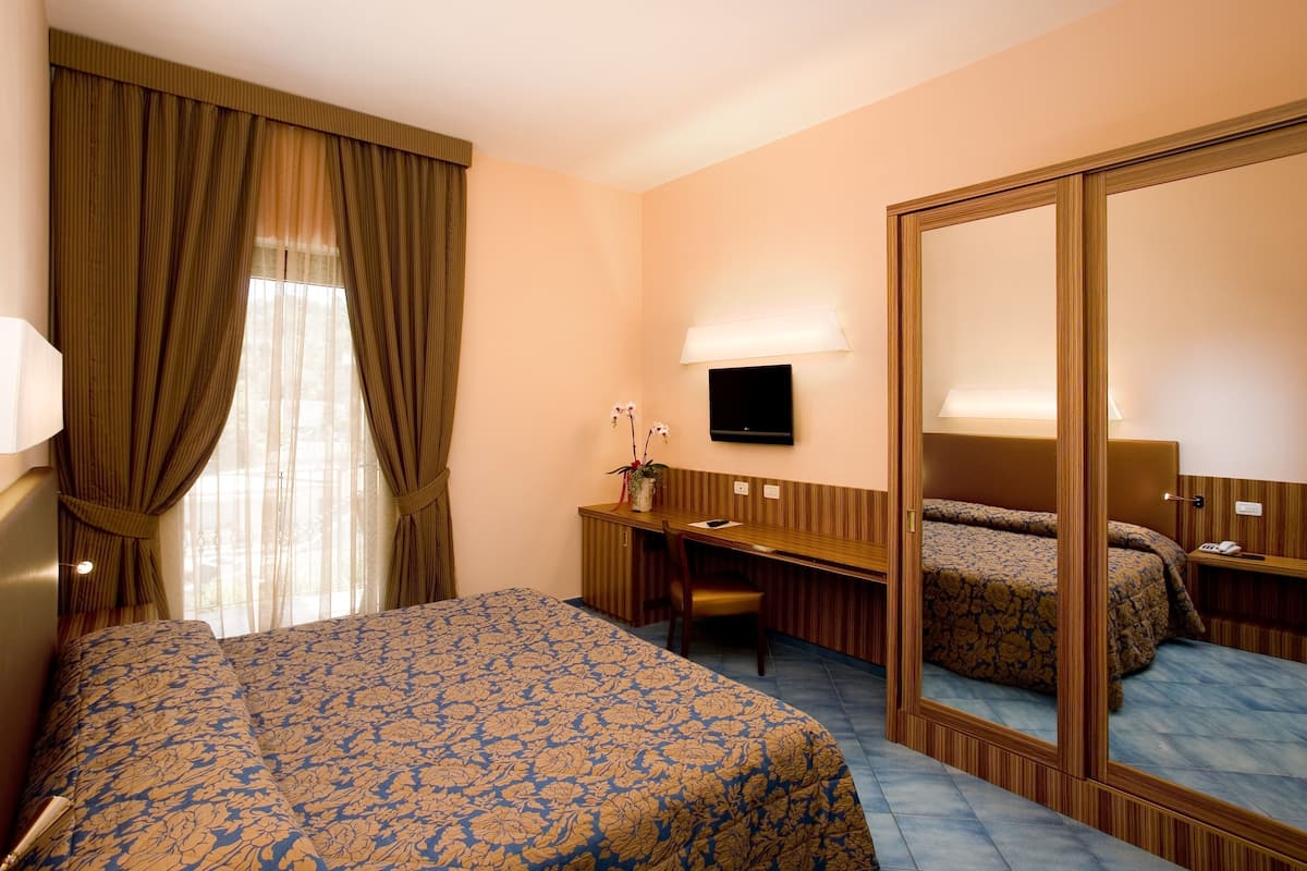 A hotel room with a bed, a desk, a chair, a TV, and a large mirror.
