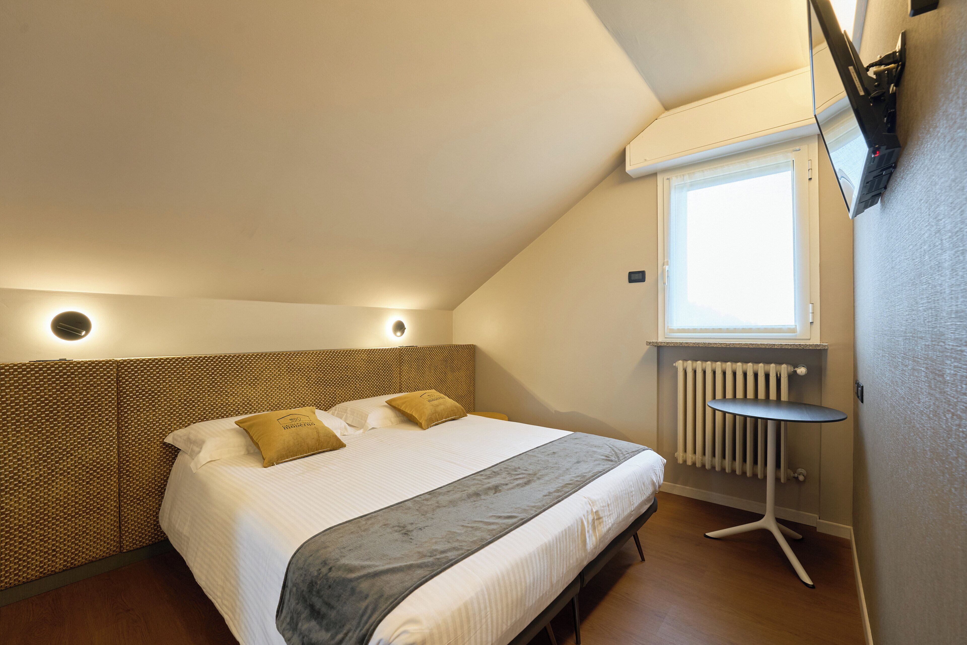 A bedroom with a bed, a bedside table, a radiator, and a window.