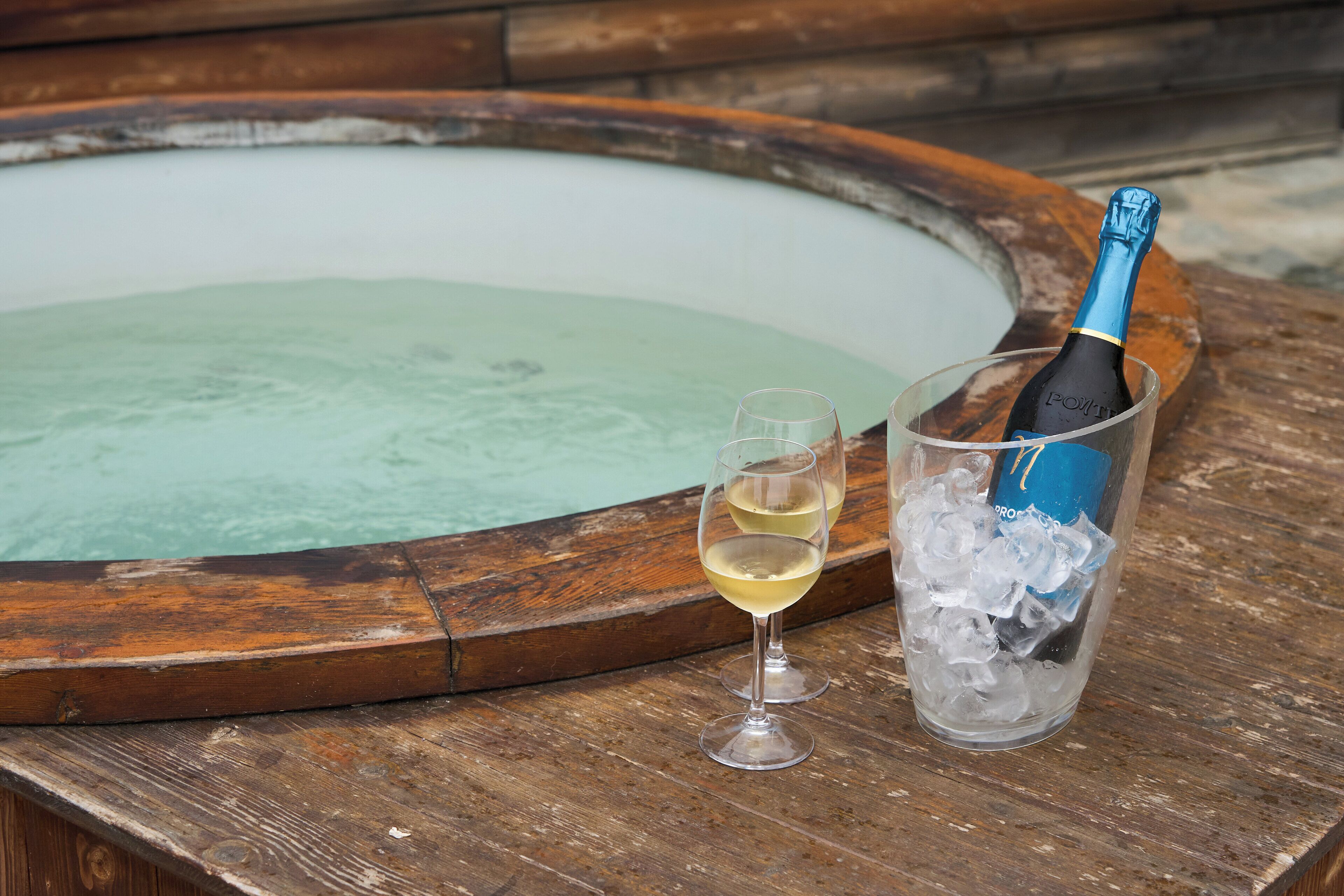 Et træbord med et glas hvidvin og en champagneflaske i en isspand.