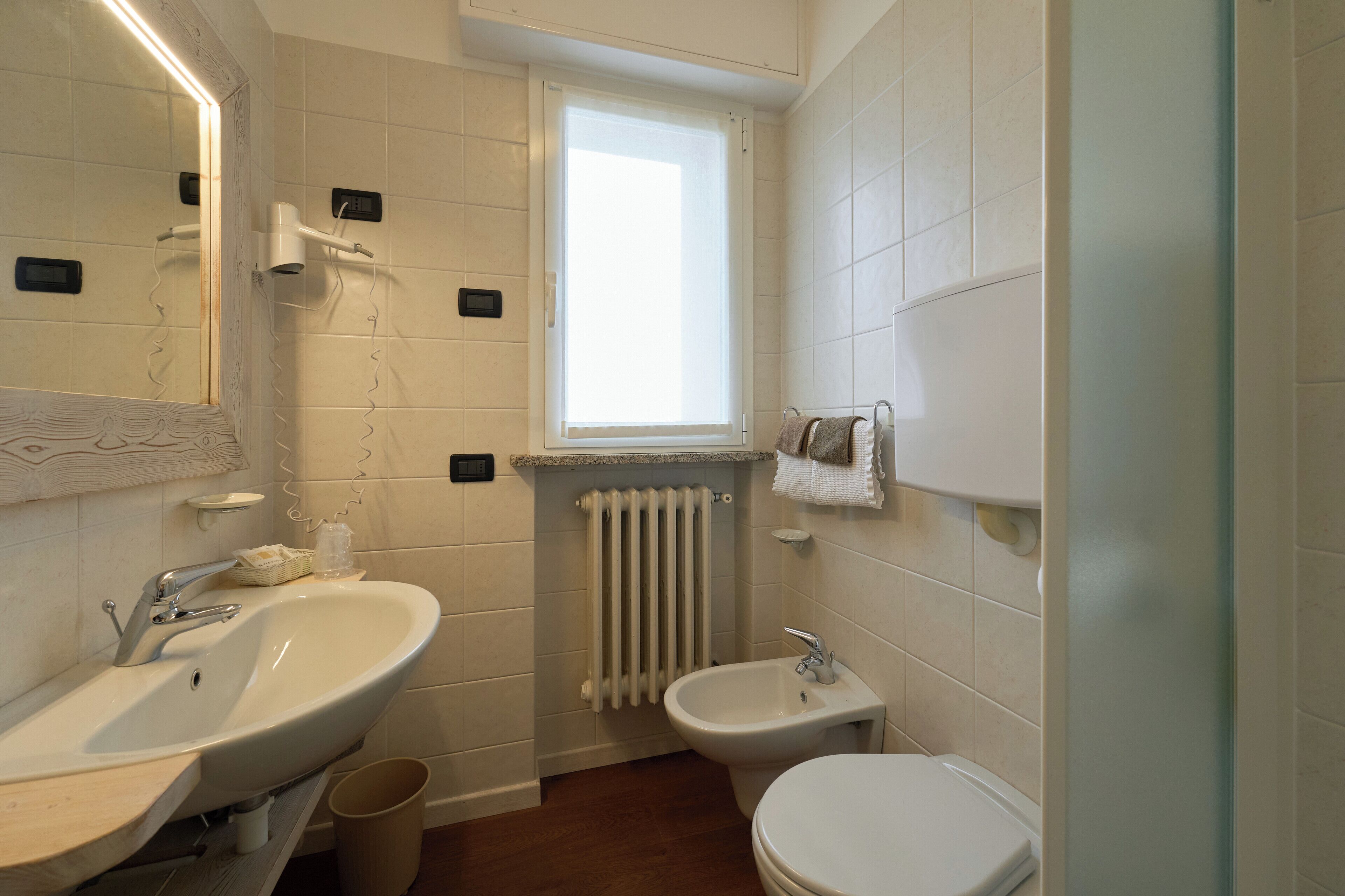A bathroom with a large mirror, two sinks, a bidet, and a window.