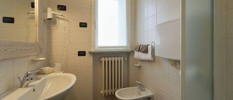 A bathroom with a large mirror, two sinks, a bidet, and a window.