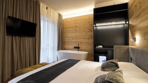 A modern hotel room with a large bed, a flat-screen TV mounted on the wall, a built-in bathtub, and a wooden accent wall. - Albergo Moderno (Fuipiano Valle Imagna)