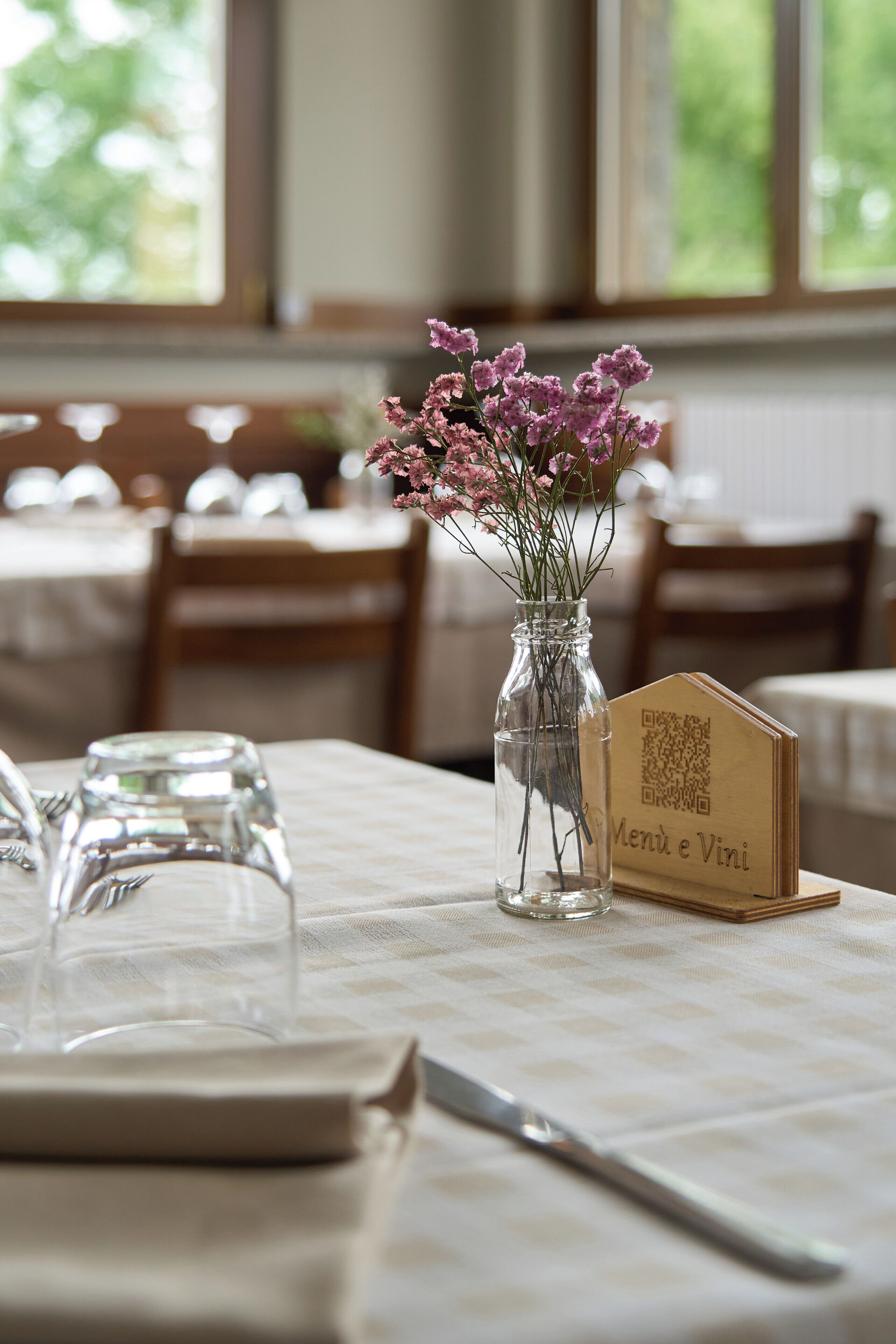 A dining table with a QR code menu, a vase with flowers, and cutlery.