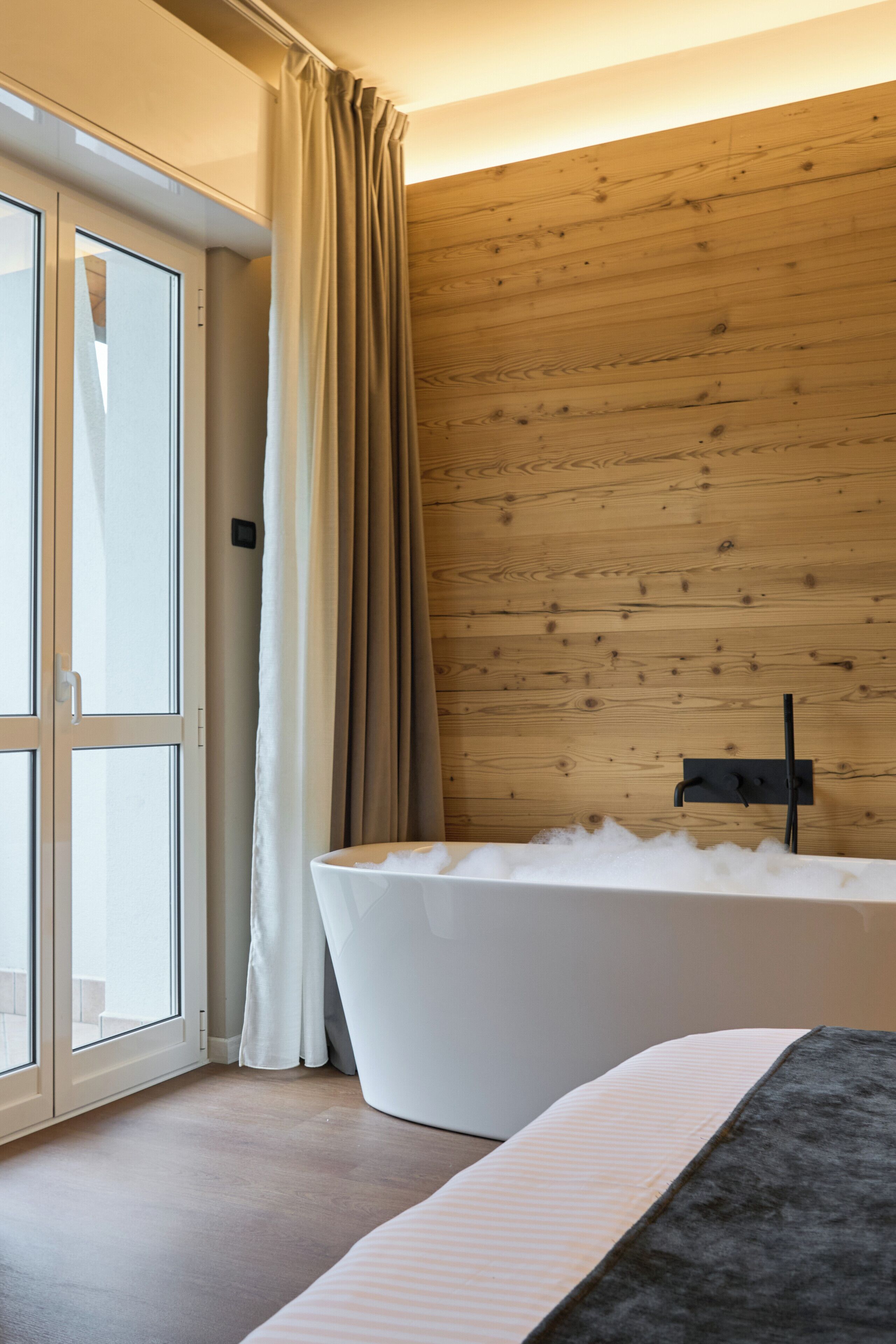 Un baño moderno con una bañera independiente, paneles de madera en las paredes y una puerta corredera de cristal que da a un espacio exterior.