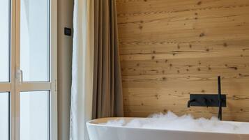 Un baño moderno con una bañera independiente, paneles de madera en las paredes y una puerta corredera de cristal que da a un espacio exterior.