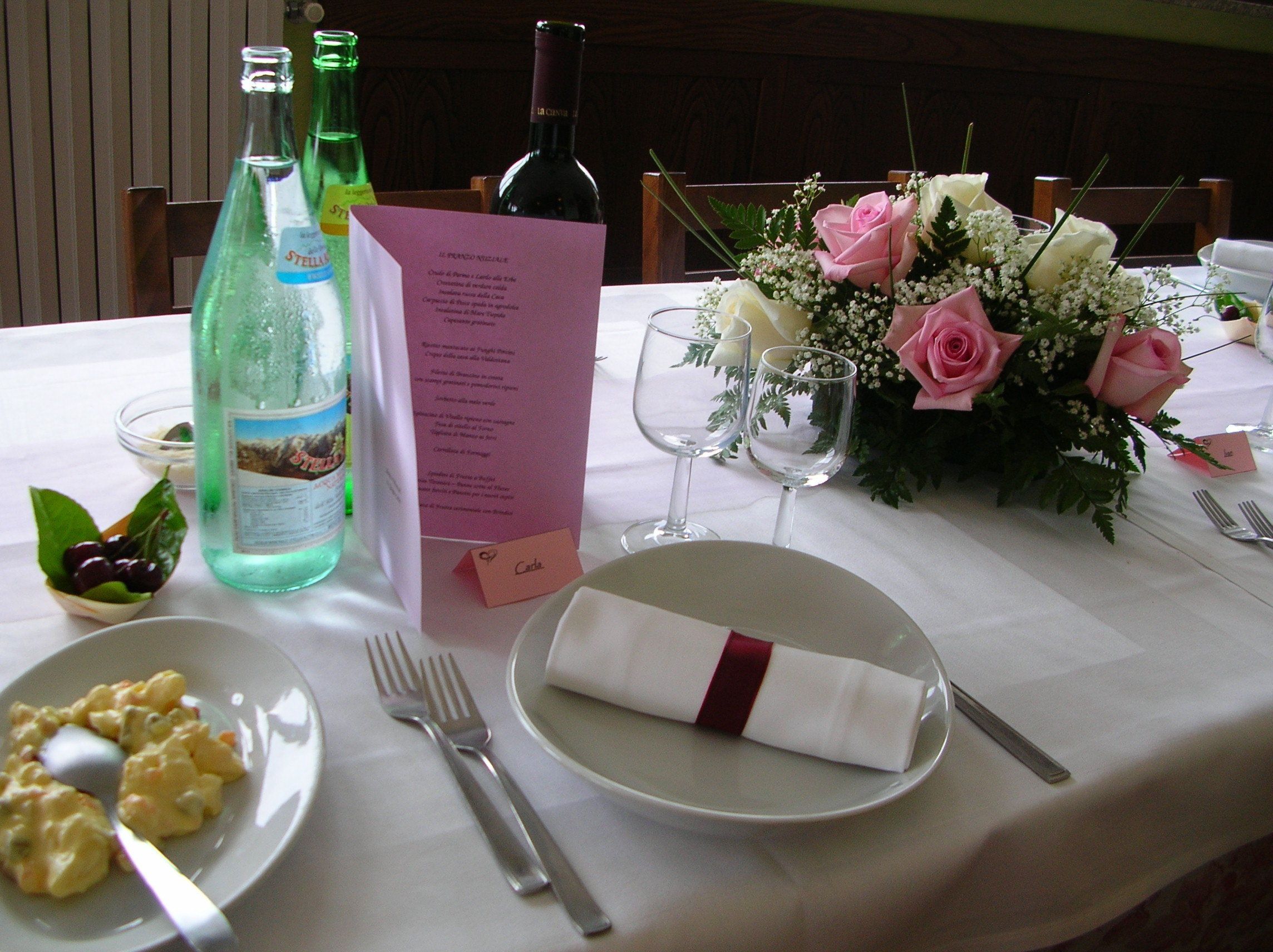 A table set for a meal with a menu, wine bottles, a flower arrangement, and a plate of food.