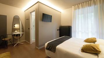 A modern hotel room with a large bed, a desk with a chair, a TV mounted on the wall, and a large window with curtains.