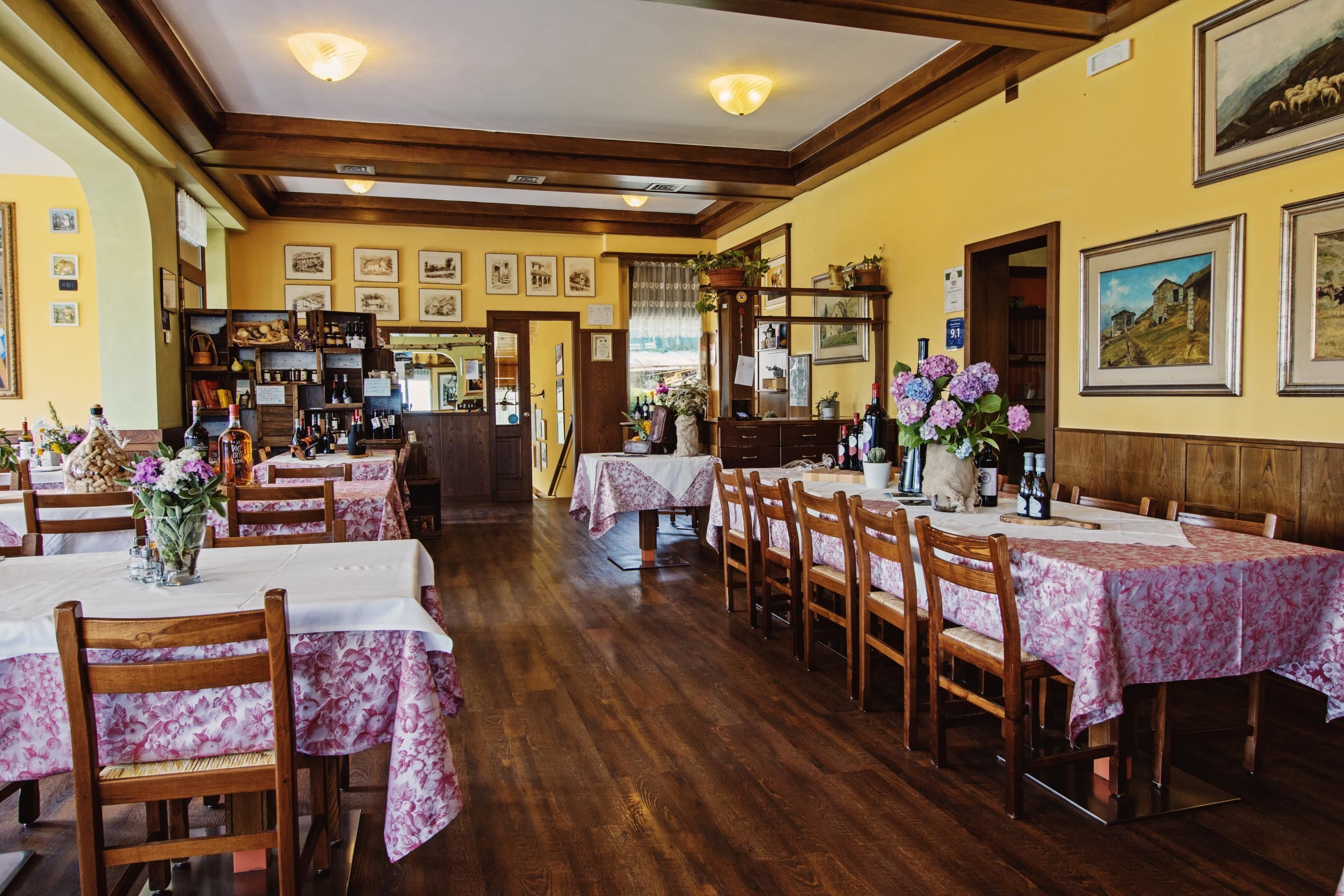 A restaurant with wooden tables and chairs, yellow walls, and framed pictures on the walls.