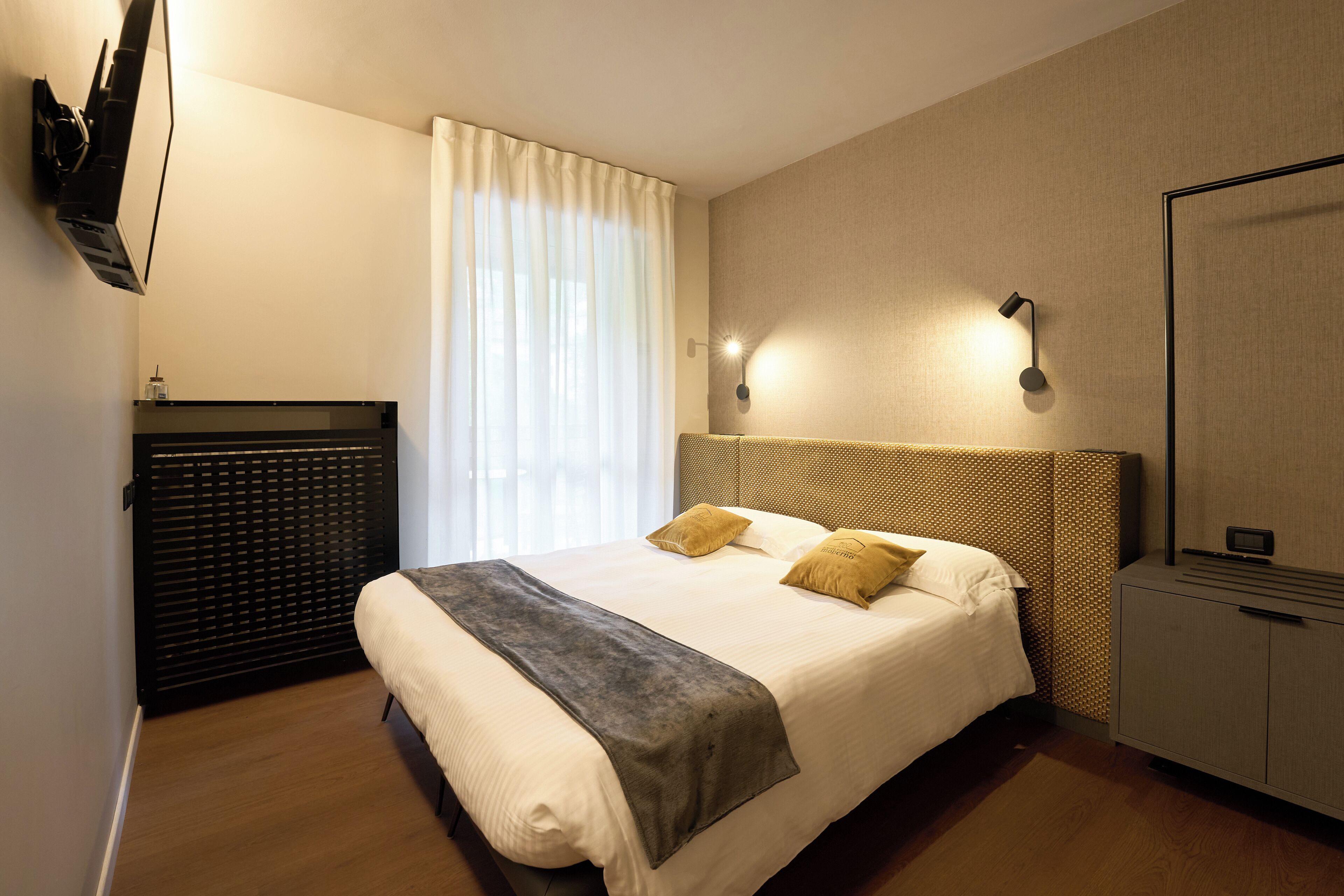 A hotel room with a large bed, a flat-screen TV mounted on the wall, a bedside table, and a wardrobe.