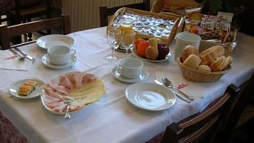 Une table de petit-déjeuner avec des assiettes de jambon, de fromage, de pain et de fruits.