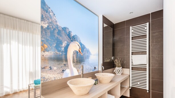Un baño moderno con un espejo grande, dos lavamanos color beige, un perchero para toallas y vista a un lago con montañas.