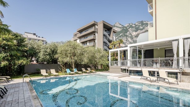 Una piscina con sillones de descanso, un área techada con barandilla y montañas al fondo.