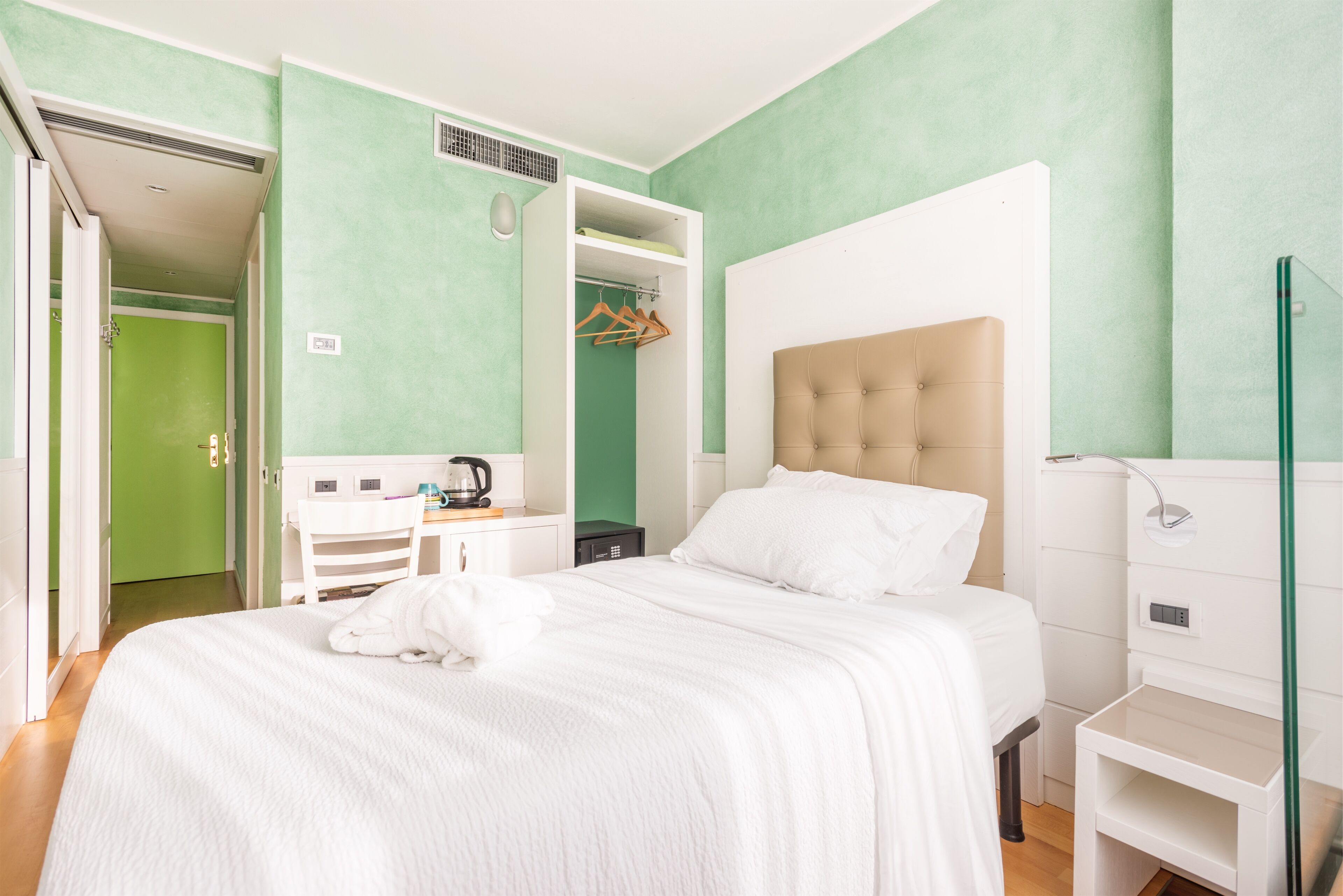 A bedroom with a bed, a wardrobe, a desk with a kettle, and a shower area.