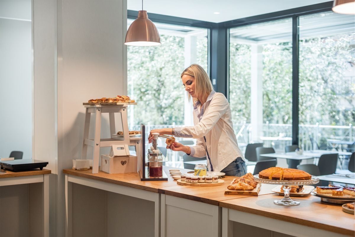 A person preparing food at a counter with various pastries and condiments.