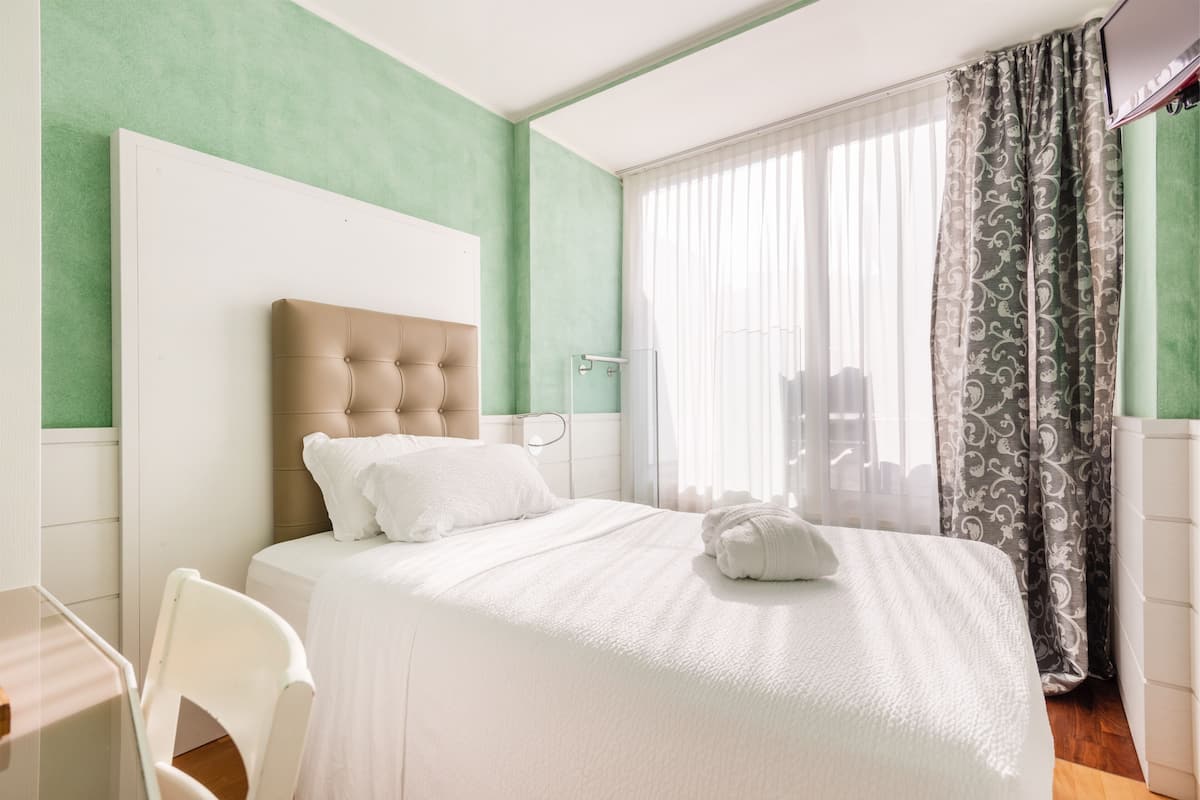 A hotel room with a large bed, a chair, a TV, and a window with curtains.