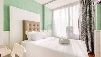 A hotel room with a large bed, a chair, a TV, and a window with curtains.