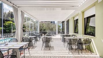 An outdoor patio area with tables and chairs, a pool, and a covered walkway.