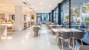 Un restaurante moderno con una barra alargada, varias mesas para comer y vistas al exterior a través de amplios ventanales.