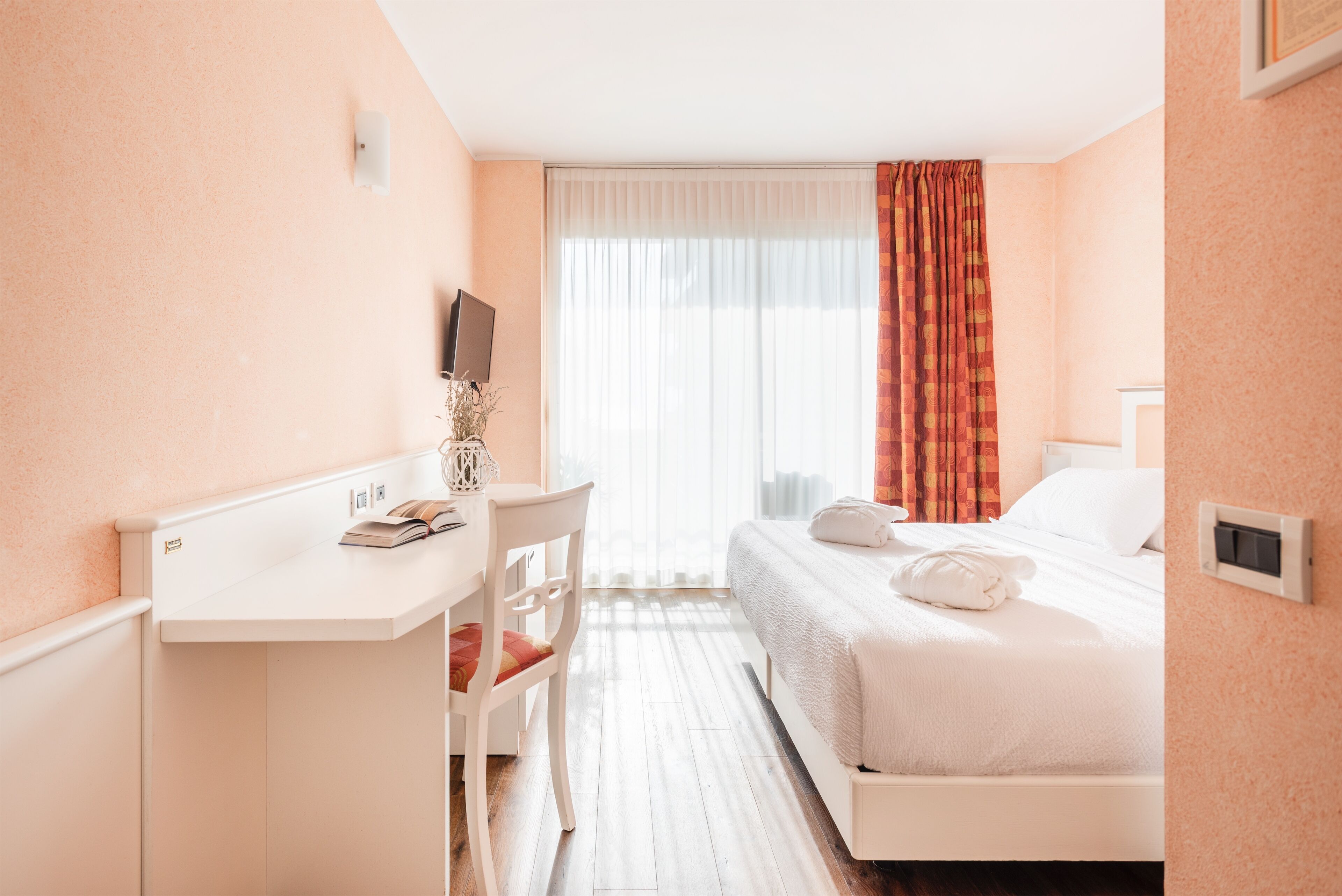A hotel room with a bed, a desk, a chair, a TV, and a window with curtains.