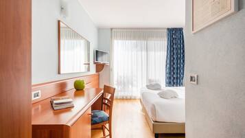 A hotel room with a wooden desk, a chair, a bed, a TV, and a window with curtains.