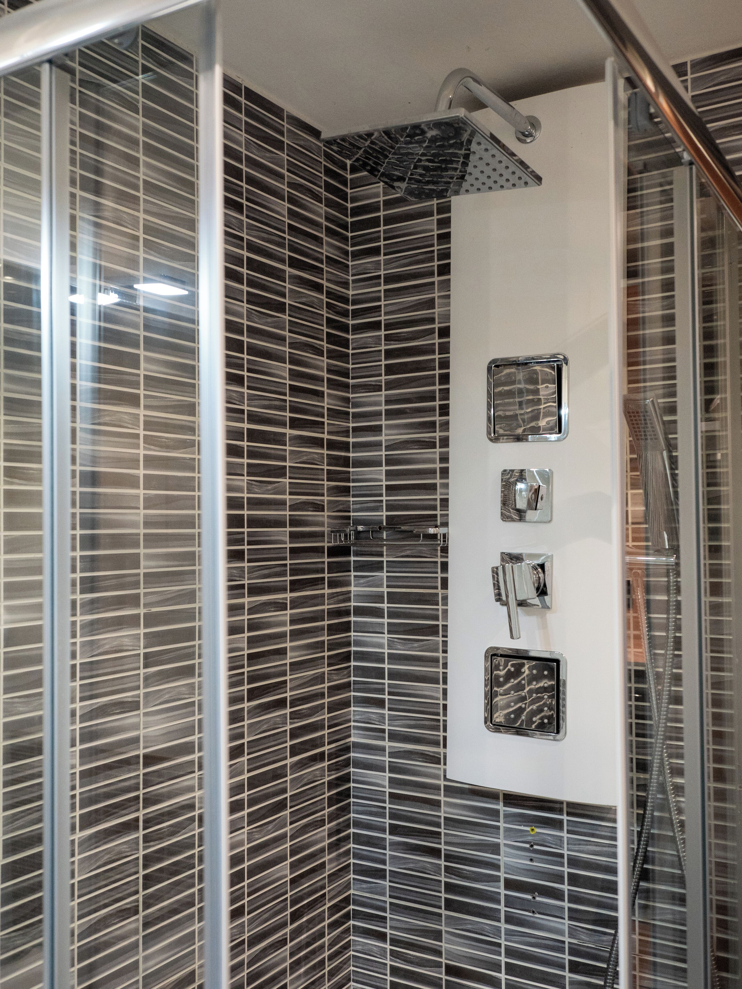 Um chuveiro com porta de vidro, um chuveiro manual e painel de controle na parede.