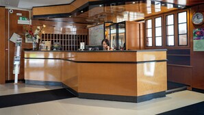 A reception desk with a wooden finish, a clock, and a calendar on the wall. - Hotel Ilga (Collecchio)